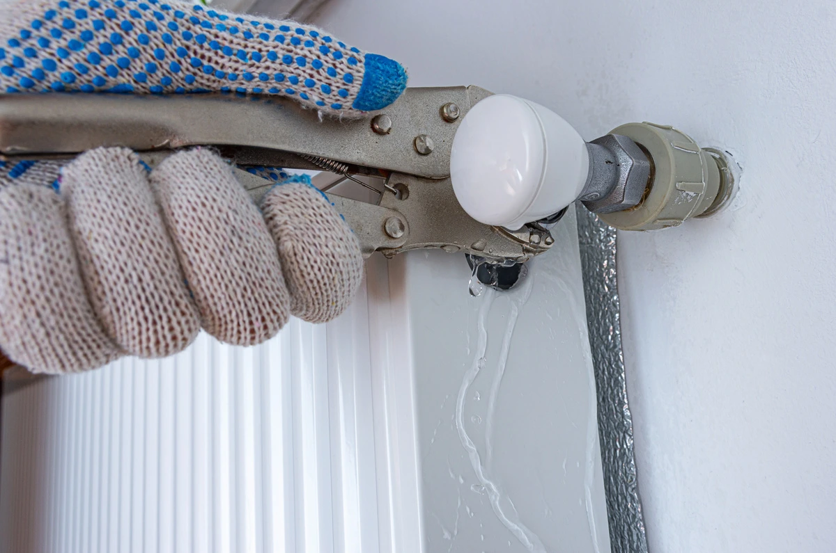 Plombier réparant une fuite d'eau au niveau d'un radiateur avec une clé à molette